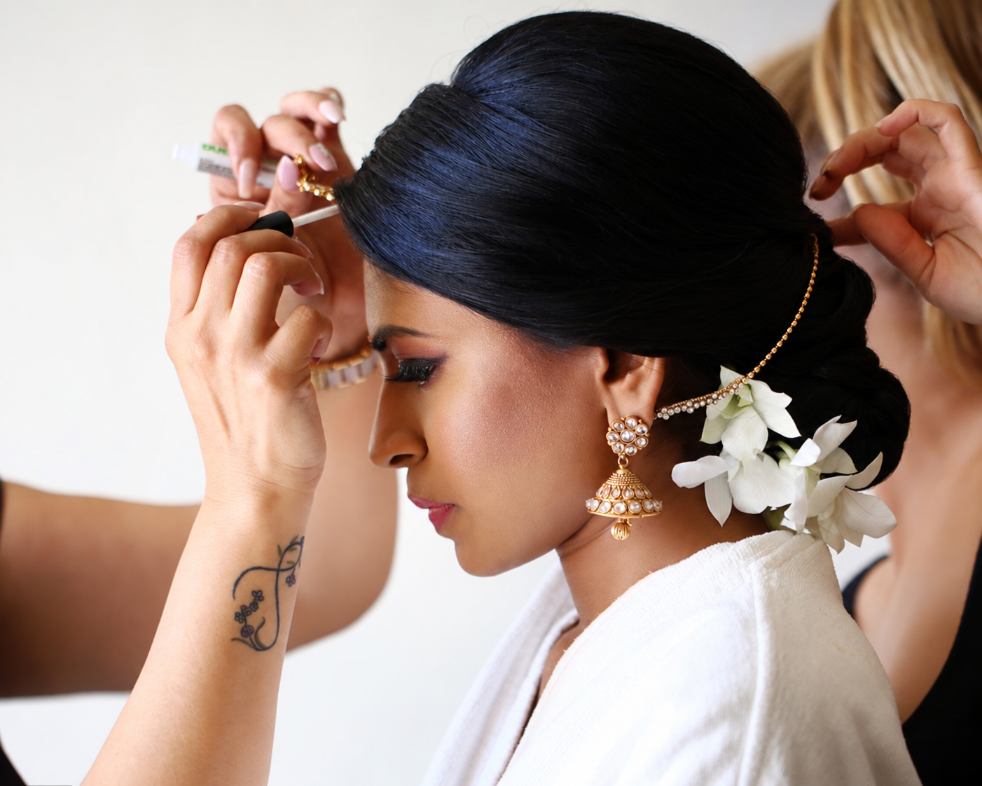 Artistas dando los últimos toques al maquillaje y al chongo adornado con flores de una novia